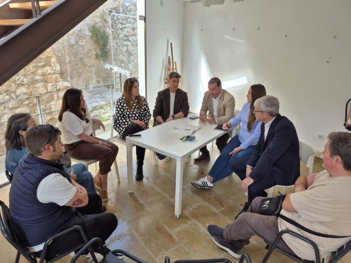 Group of seven adults seated around a white table in a bright room, discussing documents.