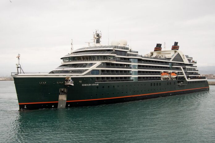 Luxurious dark-green luxury cruise ship anchored near a harbor, Seabourn Venture, with multiple decks and orange lifeboats visible along the side