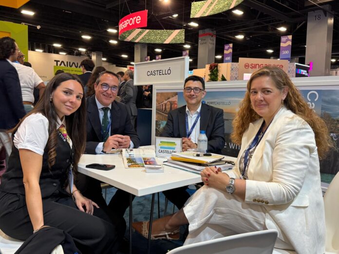 Four professionals sit around a booth table at a trade show, CASTELLÓ display behind them and brochures on the table.