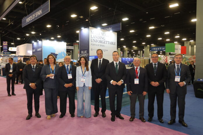 Group of professionals posing together at a trade show, standing on purple carpet with booths in the background and a 'Port of Spain' sign above.