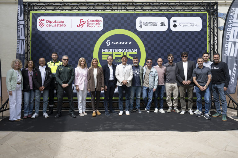 Group of adults standing shoulder to shoulder on a stage in front of a blue checkered backdrop with sponsor logos.