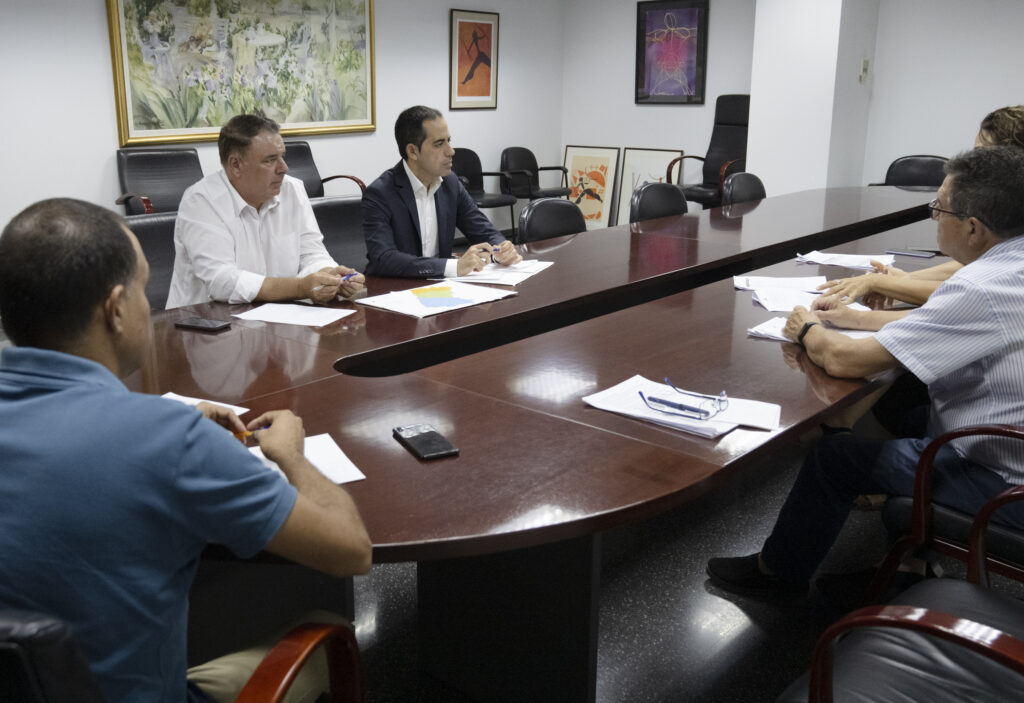 Professionals seated around a long conference table reviewing documents in a meeting room.
