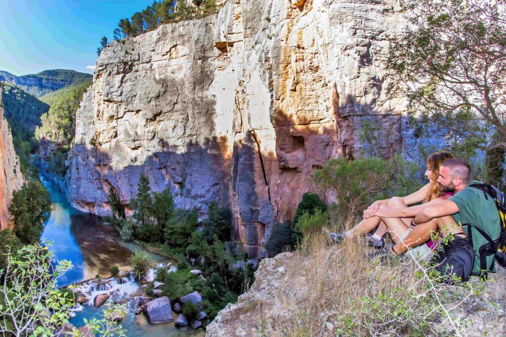 Hikers resting on a rocky cliff overlooking a turquoise river and canyon walls.