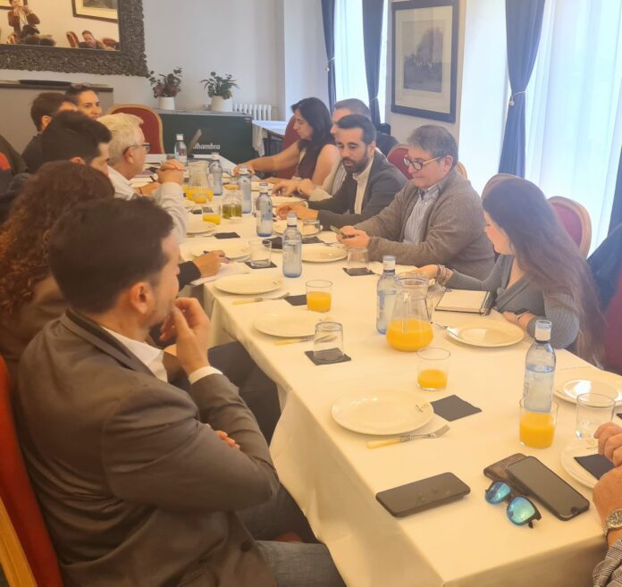 Group of people seated around a long table in a meeting room, with drinks, papers, and phones in front of them.