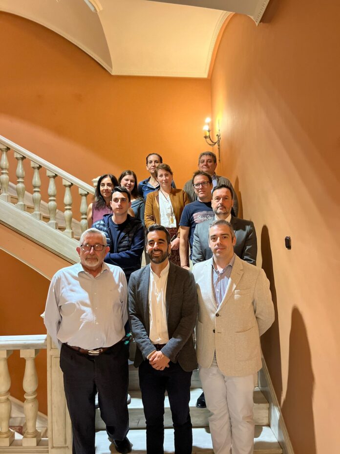 Diverse group of adults posing on a white staircase with orange walls and warm lighting for a group photo.