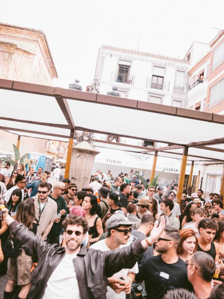 Crowded street party under a white canopy with people mingling and dancing, urban buildings in the background