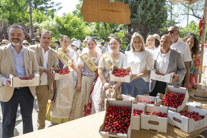 Smiling crowd at an outdoor festival with crates of cherries in the foreground.