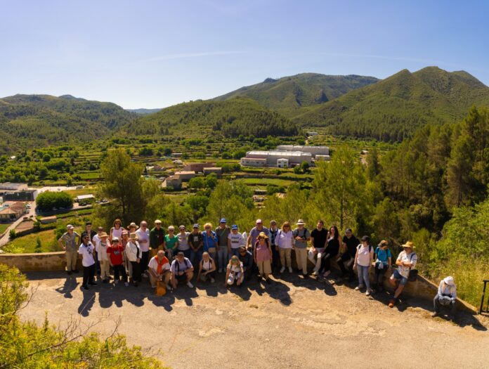 Group of hikers posing for a photo on a hillside overlook with a green valley and forested mountains in the background.