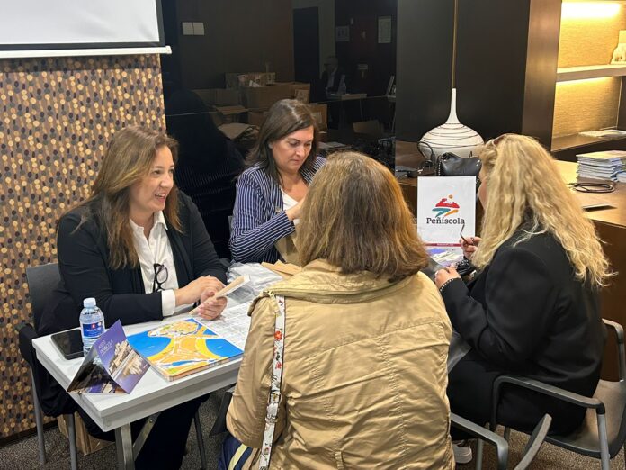 People seated around a table at a booth with brochures and maps, discussing and looking at papers. A bottle of water is visible on the table.