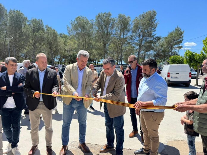 Group of men and a boy at a ribbon-cutting ceremony outdoors on a sunny day, cutting an orange ribbon together while others watch.