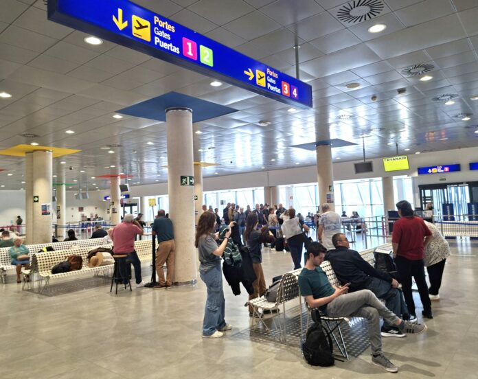 Busy airport terminal with blue overhead signs directing to gates 1–4 and passengers waiting nearby.