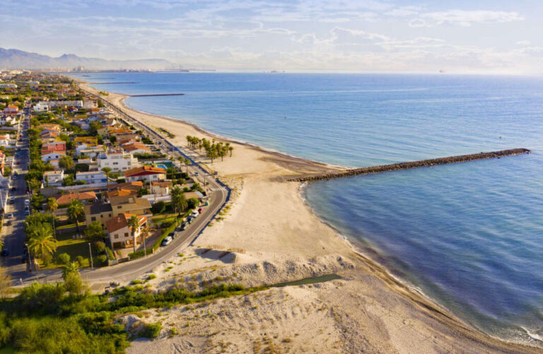 Aerial view of a coastal town with a sandy beach, calm blue sea, and a long breakwater jetty extending into the water.