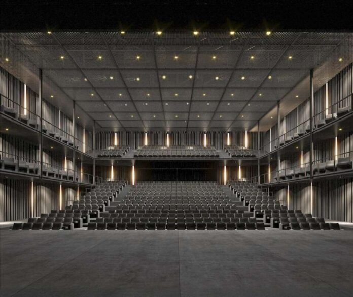 Empty modern theater with tiered rows of black seats facing a dark stage, warm wall lights.