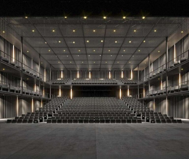 Empty modern theater with tiered rows of black seats facing a dark stage, warm wall lights.