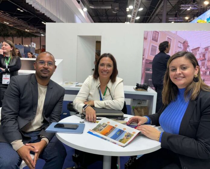 Three professionals sit around a white round table at a trade show booth, reviewing a brochure together.