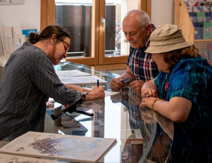 Three seniors at a glass counter looking at maps and brochures inside a shop/office.