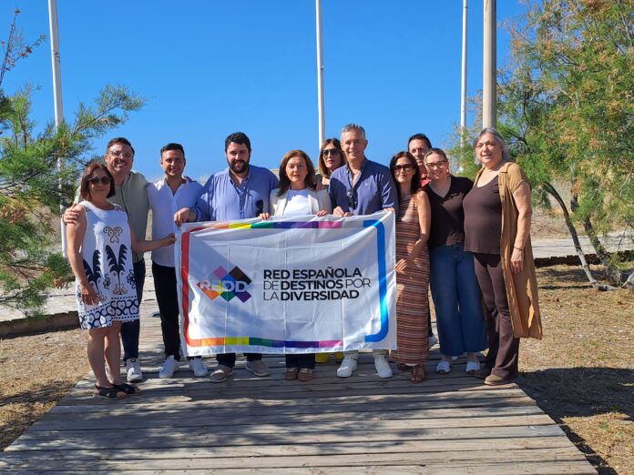Group of people holding a banner outdoors on a sunny day, promoting diversity with a rainbow border design.
