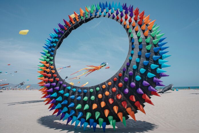 Colorful circular sculpture covered in multicolored cones on a beach.