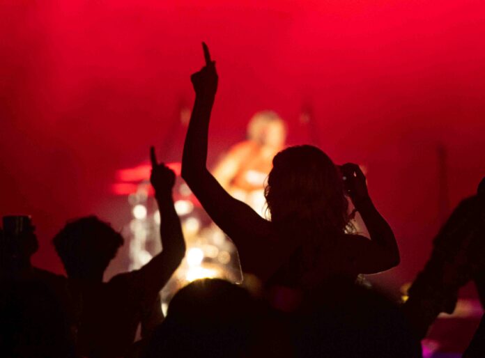 Silhouetted concert crowd with raised hands against red stage lighting, enjoying a live performance.