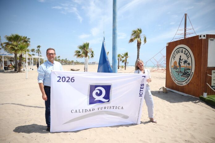 Two people stand on a sandy beach holding a large banner that reads '2026' and 'CALIDAD TURISTICA' with a purple logo in the center.