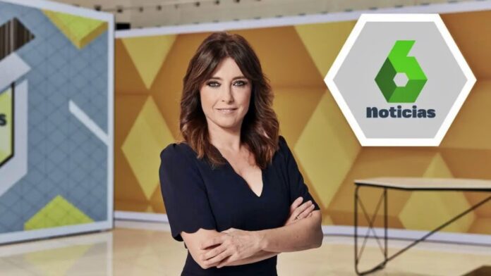 News anchor wearing a navy dress stands in a yellow geometric TV studio with the Noticias logo visible in the background.