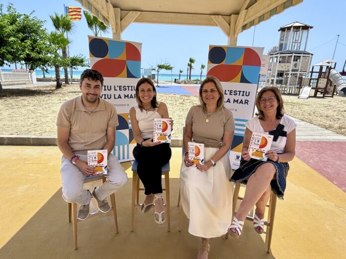 Four smiling adults sit on stools at a beach event, holding brochures with bright graphics, ocean and palm trees in the background.