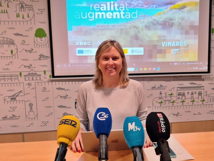 Smiling woman seated at a press conference with five colorful microphones in front; screen behind shows an augmented reality presentation.