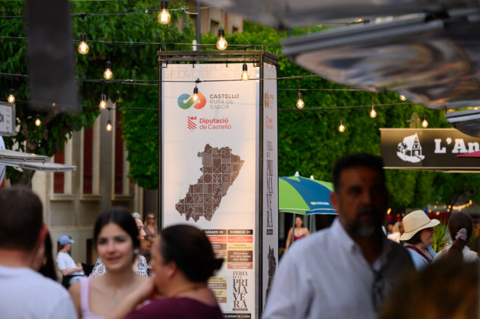 Street festival scene with hanging bulbs and a banner promoting Castelló Ruta de Sabor; crowd in foreground.