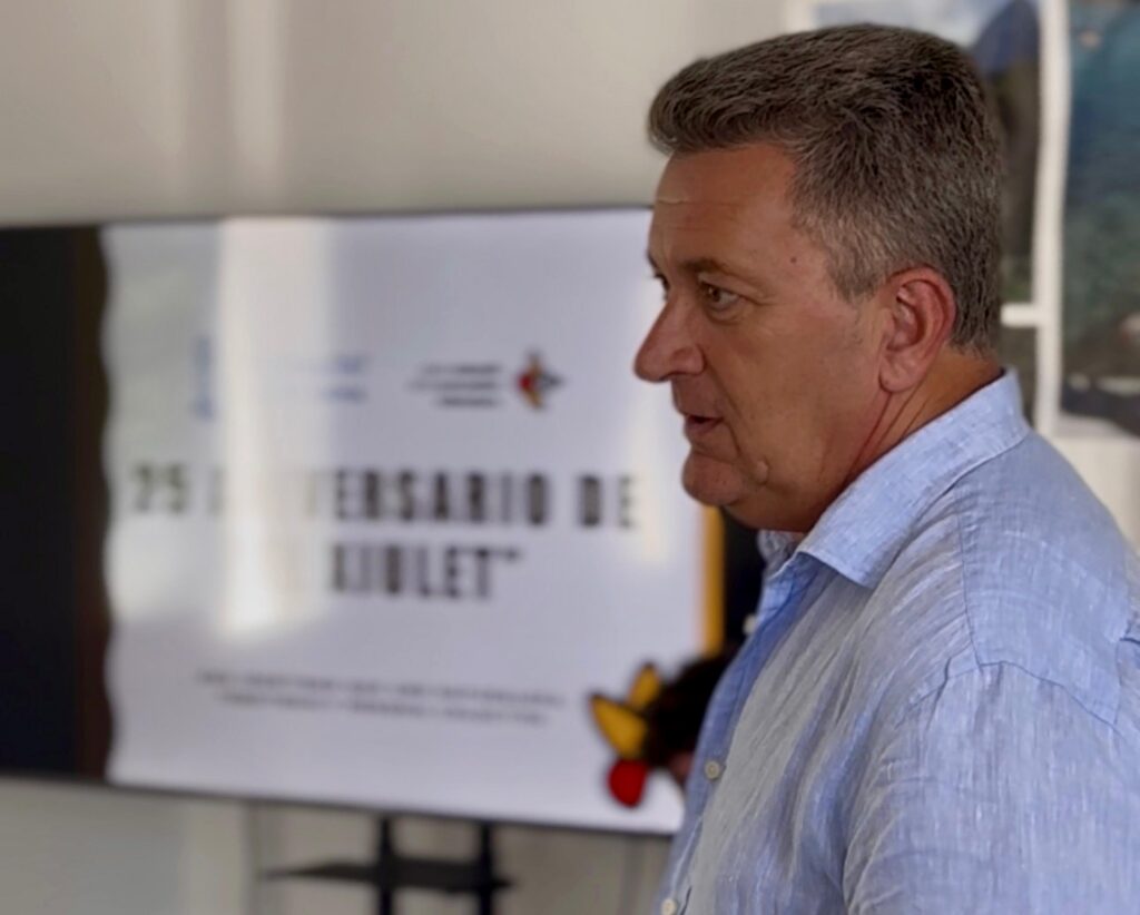 Side profile of a man in a light blue shirt facing right, indoors with a blurred poster in the background.
