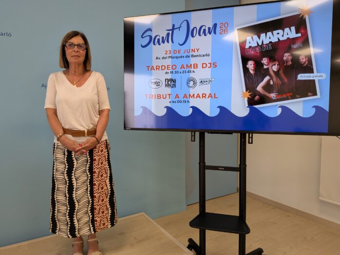 Woman in a white top and patterned skirt stands beside a large display screen showing event posters on a blue wall tone background.