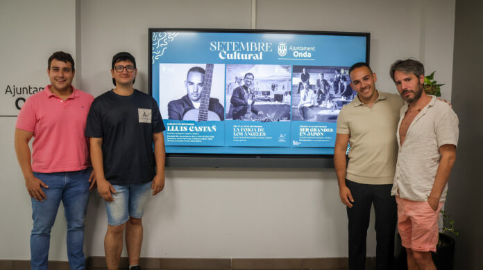 Five men pose indoors in front of a large blue display promoting cultural events.