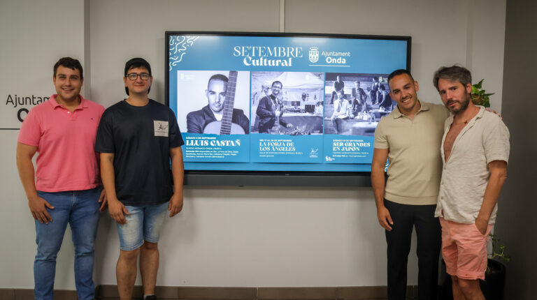 Five men pose indoors in front of a large blue display promoting cultural events.