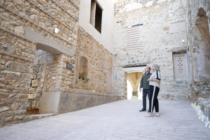 Two adults stand together in a sunlit stone alley, looking up at ancient brick walls and arches.