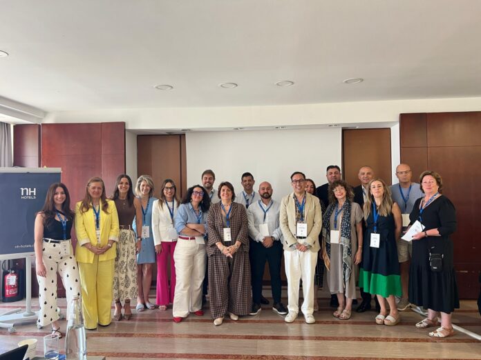 Group of professionals posing for a conference photo in a hotel lobby, with an NH Hotels banner visible on the left.