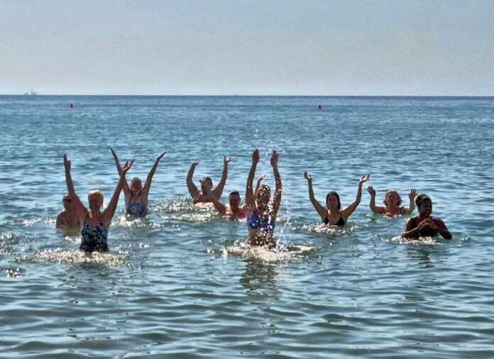 Group of people in waist-deep water at the beach, arms raised in celebration.