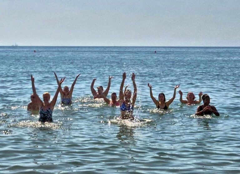 Group of people in waist-deep water at the beach, arms raised in celebration.
