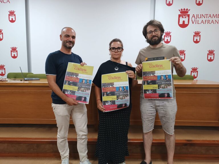 Three adults pose indoors, each holding a colorful Endins festival poster in front of a white wall with red municipal crests.