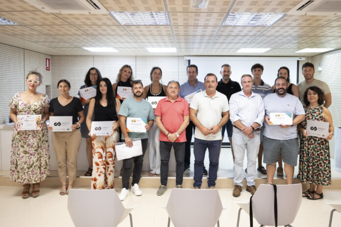 Group of men and women posing with certificates in a bright conference room with a projector screen behind them.