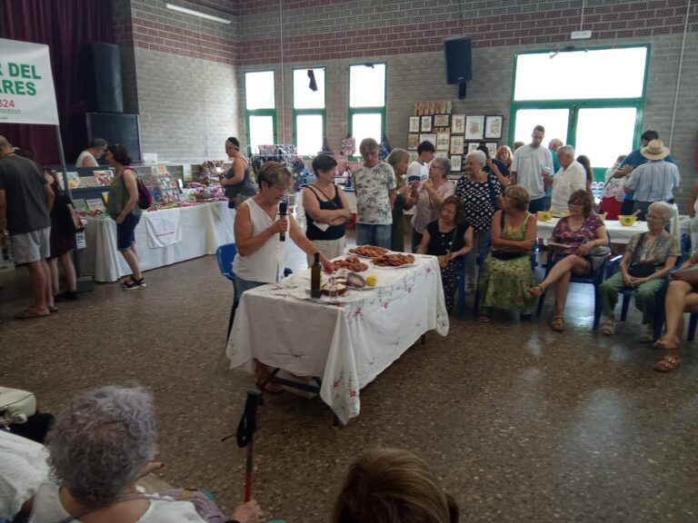 Indoor community fair with vendor tables and people browsing colorful crafts and food items on display.