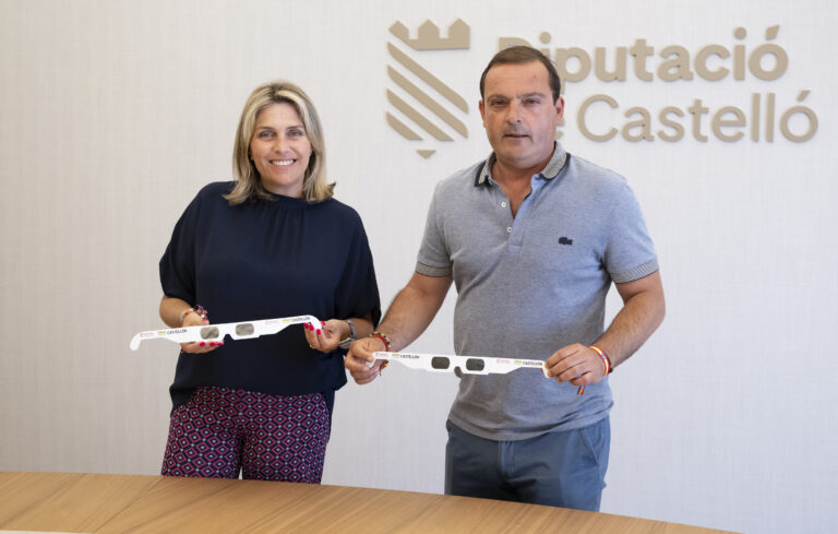 Two adults stand side by side indoors, each holding a long white strip with logos and the word Castellón in front of a wall sign.