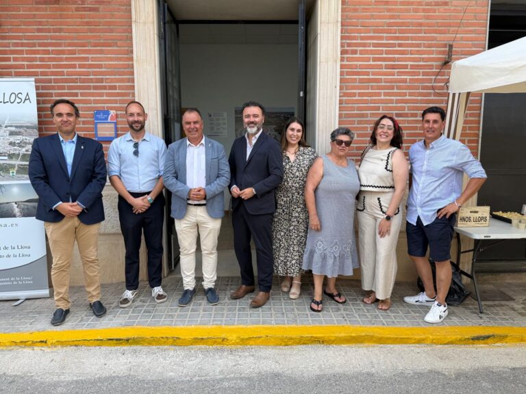Eight adults in smart casual attire pose outside a brick building for a group photo at an event.