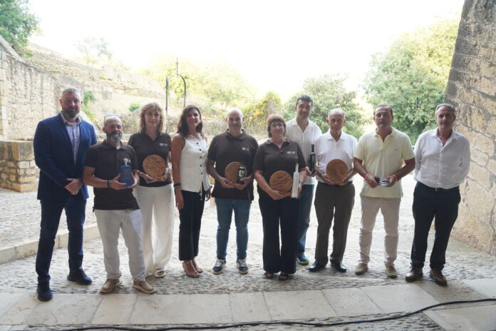 Group of ten adults standing in a stone courtyard, posing with wooden plaques and bottles as awards.