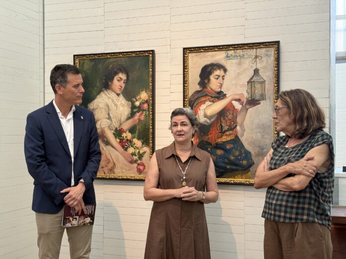 Four adults stand in an art gallery in front of two large framed paintings on a light paneled wall.