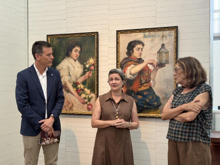 Four adults stand in an art gallery in front of two large framed paintings on a light paneled wall.