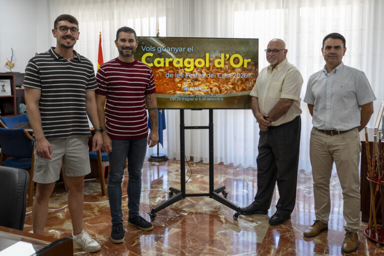 Four men stand beside a screen displaying the Caragol d’Or festival banner for Festes del Crist 2026.