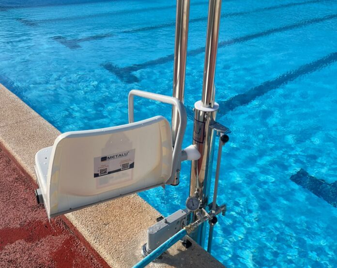 Pool accessibility lift chair attached to a metal frame at the pool edge beside bright blue water.
