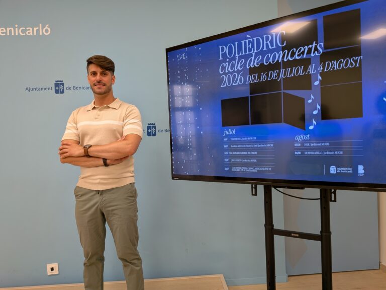 Man standing with arms crossed beside a large digital screen showing a concert schedule on a blue wall backdrop.