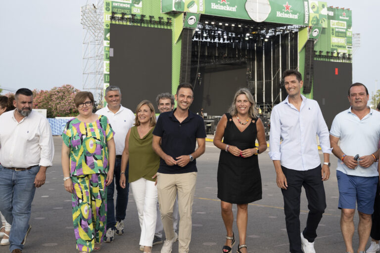 Eight adults posing for a photo in front of a large outdoor concert stage with green Heineken branding.